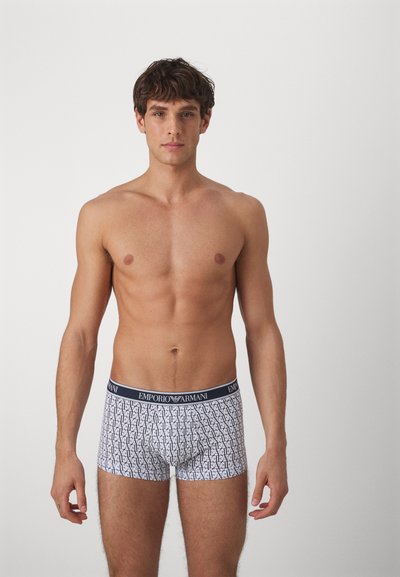 Pánske biele boxerky so čiernymi geometrickými vzormi, elastický pás Emporio Armani a priliehavý strih, ktorý ukazuje hladkú textúru materiálu.