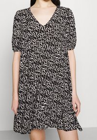 Robe courte à manches courtes noire et crème avec un décolleté en V, une jupe à volants et un motif abstrait. Fabriquée en tissu léger avec une coupe décontractée.