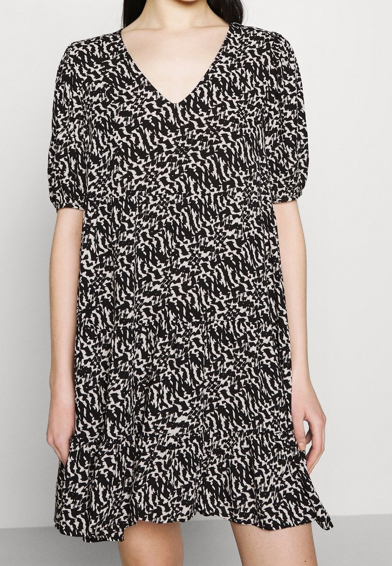 Robe courte à manches courtes noire et crème avec un décolleté en V, une jupe à volants et un motif abstrait. Fabriquée en tissu léger avec une coupe décontractée.