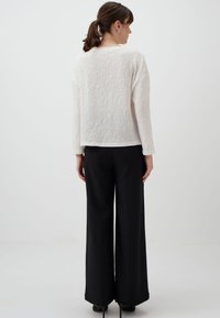 Witte gebreide trui met een bloemmotief, gecombineerd met zwarte wijde broekspijpen. De outfit heeft lange mouwen en een ontspannen pasvorm.