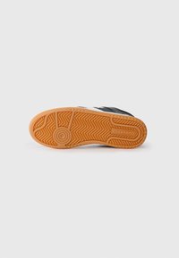Svart og hvit sneakersåle med fiskebensmønster; gummierte tekstur; oransje yttersåle med sirkulært logo-detalj.