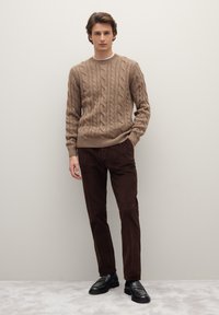 Suéter marrón de punto trenzado combinado con pantalones de pana marrón oscuro y mocasines de cuero negros. Detalles texturizados de punto visibles en el diseño del suéter.