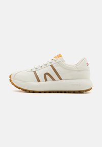 Vit sneaker med bruna ränder och orange accent, med en tjock sula och rund tå. Texturerad ovandel med snörning och varumärkesdetalj.