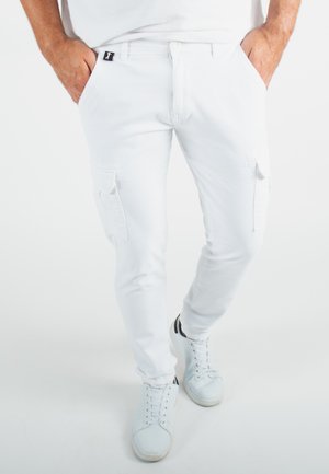 Pantalons cargo blancs à coupe slim, dotés de multiples poches, d'une fermeture à bouton et d'une construction élégante. Portés avec des baskets blanches.