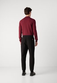 Bordeaux langemouwen shirt gecombineerd met zwarte tapered joggers met een elastische tailleband en zijzakken, afgewerkt met zwarte schoenen.