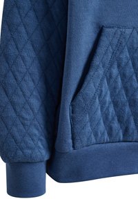 Blå hoodie med ett quiltat fickdesign, slät textur, ribbade ärmar och avslappnad passform. Rik färg med diamantmönster.