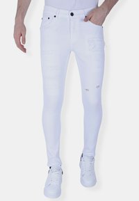 Witte skinny jeans van denim met verweerde details, voorzien van een strakke pasvorm, vijf zakken en zwarte accenten. Gecombineerd met witte sneakers.