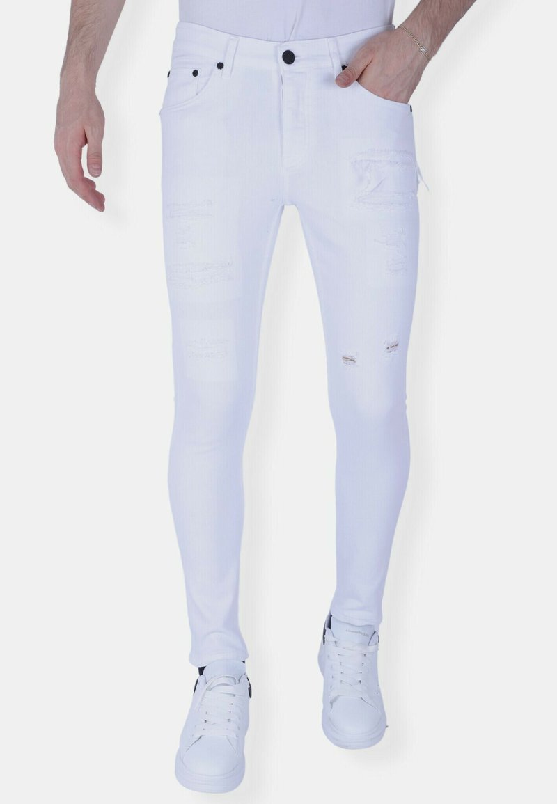 Witte skinny jeans van denim met verweerde details, voorzien van een strakke pasvorm, vijf zakken en zwarte accenten. Gecombineerd met witte sneakers.