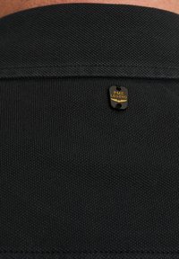 Textil negro con una superficie texturizada y una pequeña etiqueta de marca rectangular en dorado y negro, que dice "PME LEGEND" cerca del escote.