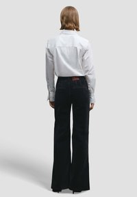 Wit overhemd met knopen en lange mouwen, gecombineerd met zwart, hoog getailleerd, wijd uitlopende broek met een achterkant zak.