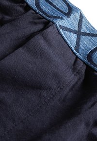 Țesătură marină cu o suprafață texturată, având un brâu din denim de culoare albastru deschis embossat cu un model de litere și curbe de culoare albastru închis.