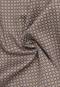Textiel met een geometrisch patroon van bruine, witte en zwarte hexagonale vormen, zachte textuur en fijne details in een stofarrangement.