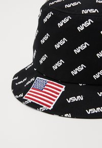 Čierny vedierkový klobúk so zopakovaným bielym textom "NASA" a vyšívanou americkou vlajkou na boku. Vyrobený z jemného materiálu.