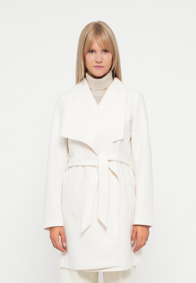 White wrap coat in soft fabric with a shawl collar, long sleeves, and a tied belt; features side pockets and a clean, minimalist design.