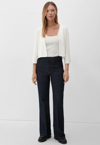 Witte cropped cardigan over een aansluitend wit topje, gecombineerd met donkerblauwe high-waisted jeans en zwarte chunky laarzen. Eenvoudig en schoon ontwerp.