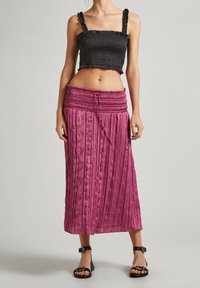 Černý krátký top s nariasením a volánikovými ramienkami; ružová plisovaná midi sukňa so zošitým pásom a šnúrkou; nosené s čiernymi sandálmi.