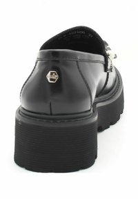 Zwarte gepatenteerde leren schoen met een chunky rubberen zool, met een zilveren accent en stikdetails langs de bovenrand.