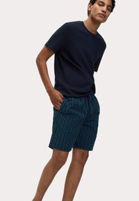 Marineblauw T-shirt met textuur gecombineerd met teal shorts met verticale witte strepen. De shorts hebben een elastische tailleband met trekkoord en zijzakken.