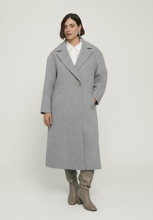 Lichtgrijze wollen jas met een gelapte kraag, zijzakken en een enkele knoopsluiting, gecombineerd met grijze slouchy hoge hakken.