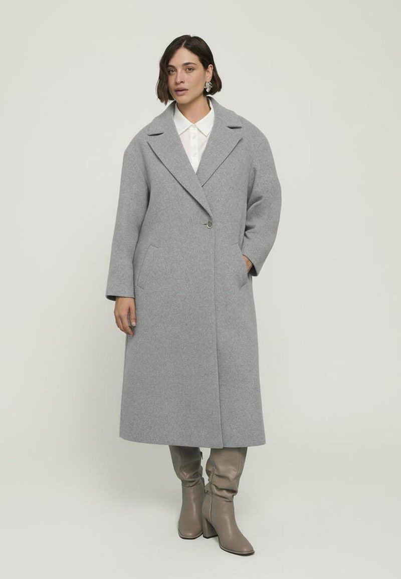 Cappotto di lana grigio chiaro con colletto a rever, tasche laterali e chiusura a singolo bottone, abbinato a stivali grigi a tacco alto e morbidi.