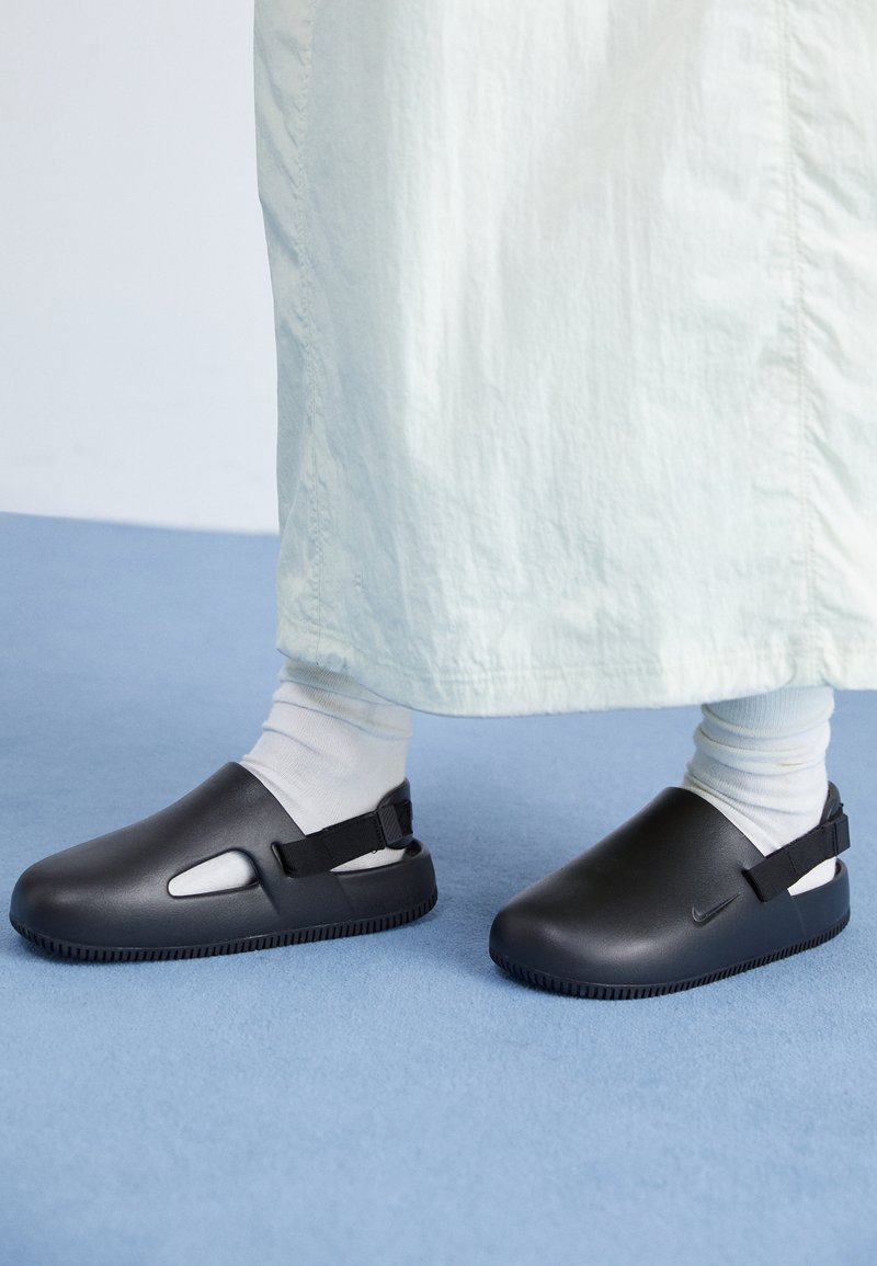 Zwarte instapschoenen van glad materiaal met een afgeronde design, voorzien van twee zijkleppen en een achterkantriem voor een veilige pasvorm.