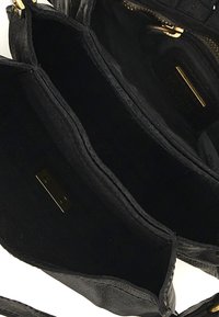 Interno di una borsa a tracolla in pelle nera, con due scomparti principali, hardware color oro e una fodera testurizzata. È visibile la chiusura con zip.