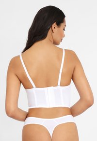 White bustier with adjustable straps and hook closure. Smooth fabric, structured design, and a fitted silhouette complementing the body shape.