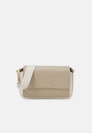Beige skuldertaske med hvide kanter, en gylden Tommy Hilfiger-logo på klappen og en bred hvid rem med beige syninger.