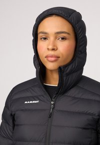 Svart puffjacka med huva, med horisontella quiltade sektioner, dragkedjestängning och Mammut-logotyp på vänster sida. Slät, matt yta.