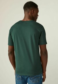 Mørkegrøn bomulds T-shirt med korte ærmer, rund halsudskæring og en glat tekstur, parret med blå jeans, set fra ryggen.