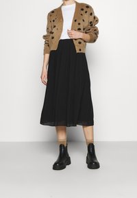 Brun, prikkeret cardigan over en hvid top, parret med en sort plisseret midi-nederdel og sorte platform ankelstøvler.