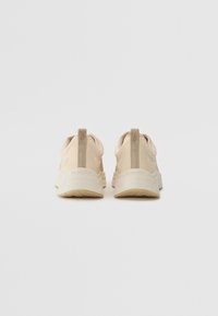 Baskets de sport beige clair avec une texture lisse et un design incurvé. Présentent un logo sur le talon et des accents beiges sur le dessus.