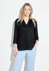 Camicia nera con colletto a V, maniche lunghe e vestibilità comoda, abbinata a pantaloni azzurri. Tessuto morbido, design semplice.