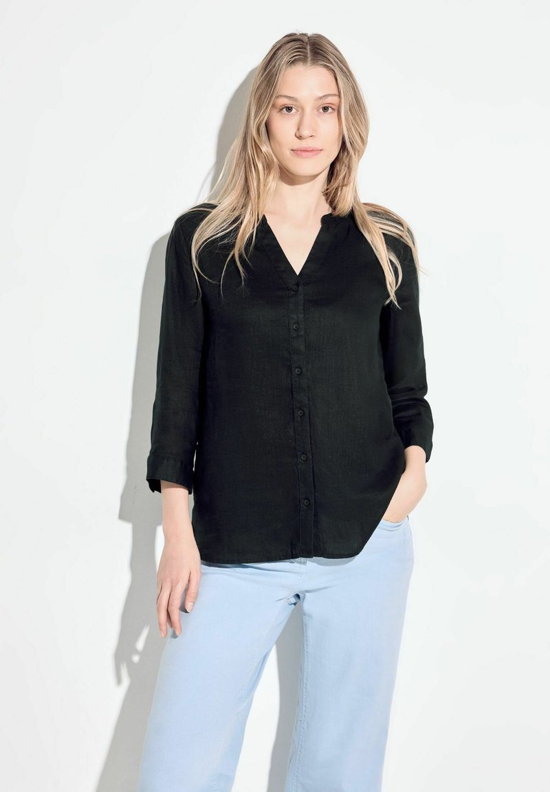 Camicia nera con colletto a V, maniche lunghe e vestibilità comoda, abbinata a pantaloni azzurri. Tessuto morbido, design semplice.