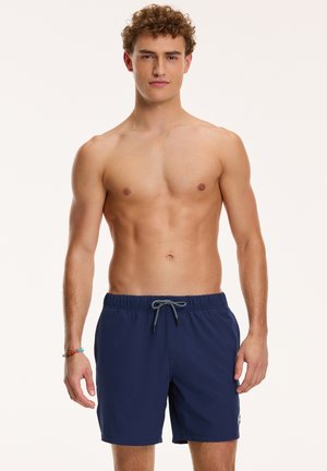 Marineblaue Badetights aus leichtem Stoff, mit einem elastischen Bund und einer Kordel sowie einem kleinen Logo-Detail am Bein.
