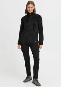 Zwart fleece pullover met een half-zip kraag en voorzakken, voorzien van een zachte textuur en een klein logo detail nabij de zoom.