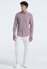 Rood-wit geblokt overhemd met lange mouwen, gecombineerd met witte broek en witte sneakers. Eenvoudige kraag en getailleerd ontwerp.