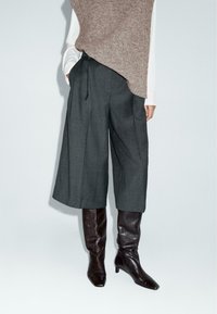 Grijze wijde broek gemaakt van een gestructureerde stof, gecombineerd met kniehoge, donkerbruine leren laarzen met een spitse neus.