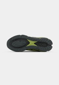 Semelle de chaussure de sport noire et verte avec motifs antidérapants texturés et un design à orteil fendu sur un fond clair uni.