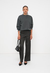 Γκρίζα φούτερ με μακριά μανίκια, συνδυασμένο με ψηλόμεσα, φαρδιά παντελόνια σε σκούρο χρώμα. Τα αξεσουάρ περιλαμβάνουν μια μικρή μαύρη τσάντα και μυτερές μπαλαρίνες.