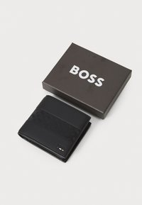Črn usnjen denarnica s teksturiranim vzorcem, prikazana delno odprta poleg rjave škatle z belim logotipom "BOSS".
