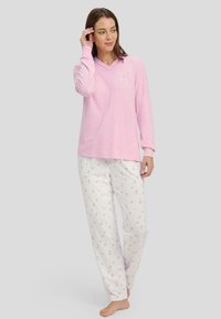 Blusa rosa de manga larga con escote en V y un pequeño gráfico, combinada con pantalones blancos que presentan un patrón de corazones en lavanda, confeccionados en una tela suave y ligera.