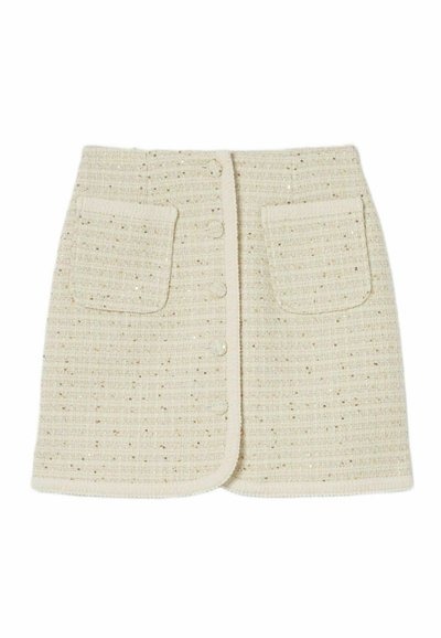 Jupe mini tissée beige en tissu texturé, avec deux poches avant et une fermeture à cinq boutons. Des éclats métalliques subtils ajoutent des détails.