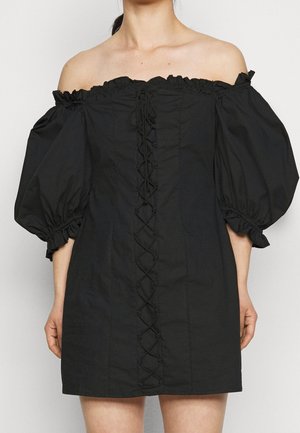 Robe noire épaules dénudées avec manches bouffantes, tissu texturé et détail central à lacets sur le devant. Bords froncés aux manches et à l'encolure.