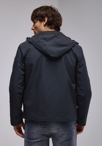 Veste résistante aux intempéries bleu marine foncé avec une capuche, présentant une texture lisse, une fermeture éclair et des poches latérales. Vue arrière affichée.