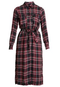 Abito camicia a quadri in nero, rosso e bianco. Presenta maniche lunghe, chiusura con bottoni frontale, due tasche sul petto e una cintura legata in vita.