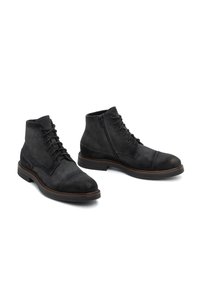 Botas de tobillo de ante negro con cierre de cordones en el frente y cremallera lateral. Puntera redondeada y costuras en contraste; suela de goma plana con un leve tacón.