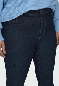 Jeans de culoare albastru închis, cu o textură fină, având talie înaltă, detalii subtile de cusătură și un design standard cu cinci buzunare.