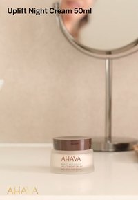 Crema Notturna Uplift AHAVA, 50ml. Il barattolo presenta una base trasparente e rotonda con una consistenza di crema bianca e un coperchio marrone scuro. L'etichetta include il nome del marchio e del prodotto.