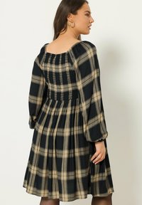 Vestido de cuadros en negro y beige con corpiño fruncido, mangas largas abullonadas y falda acampanada. Está hecho de una tela ligera con una textura suave.